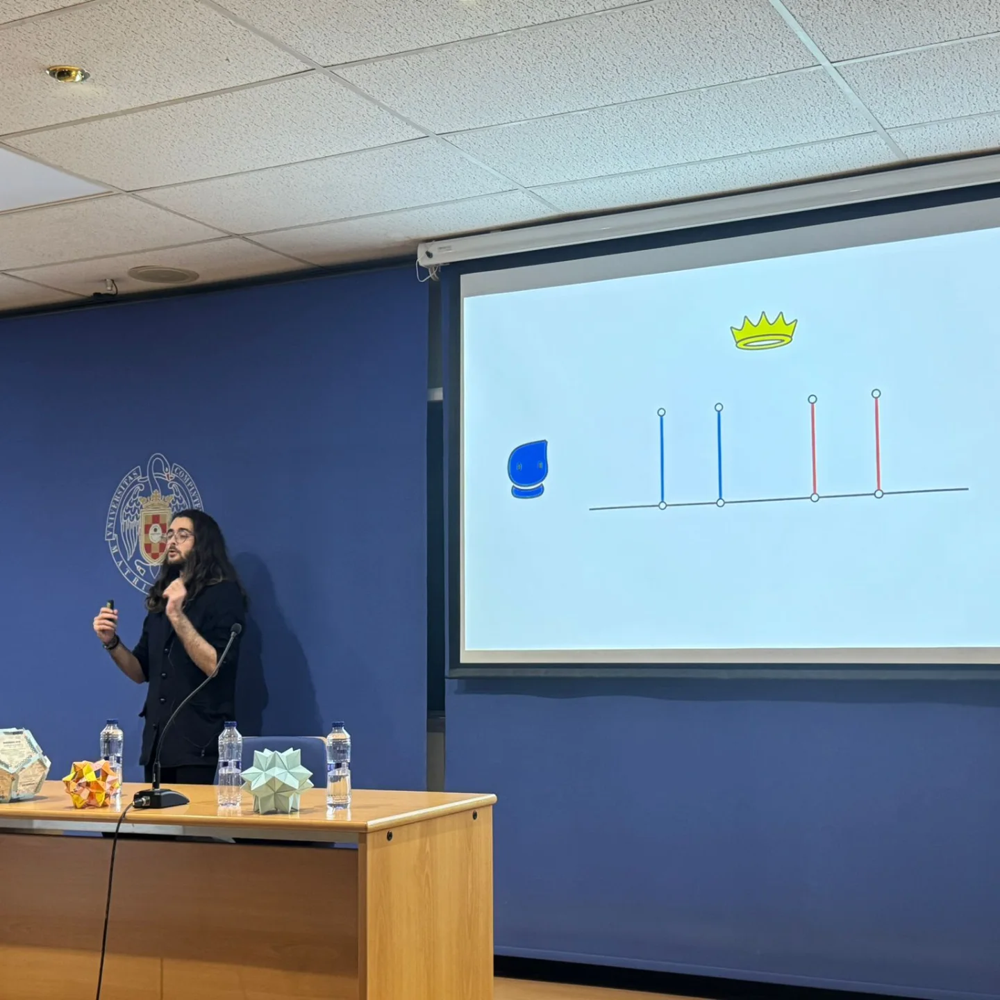 Persona hablando junto a una proyección con una representación matemática.